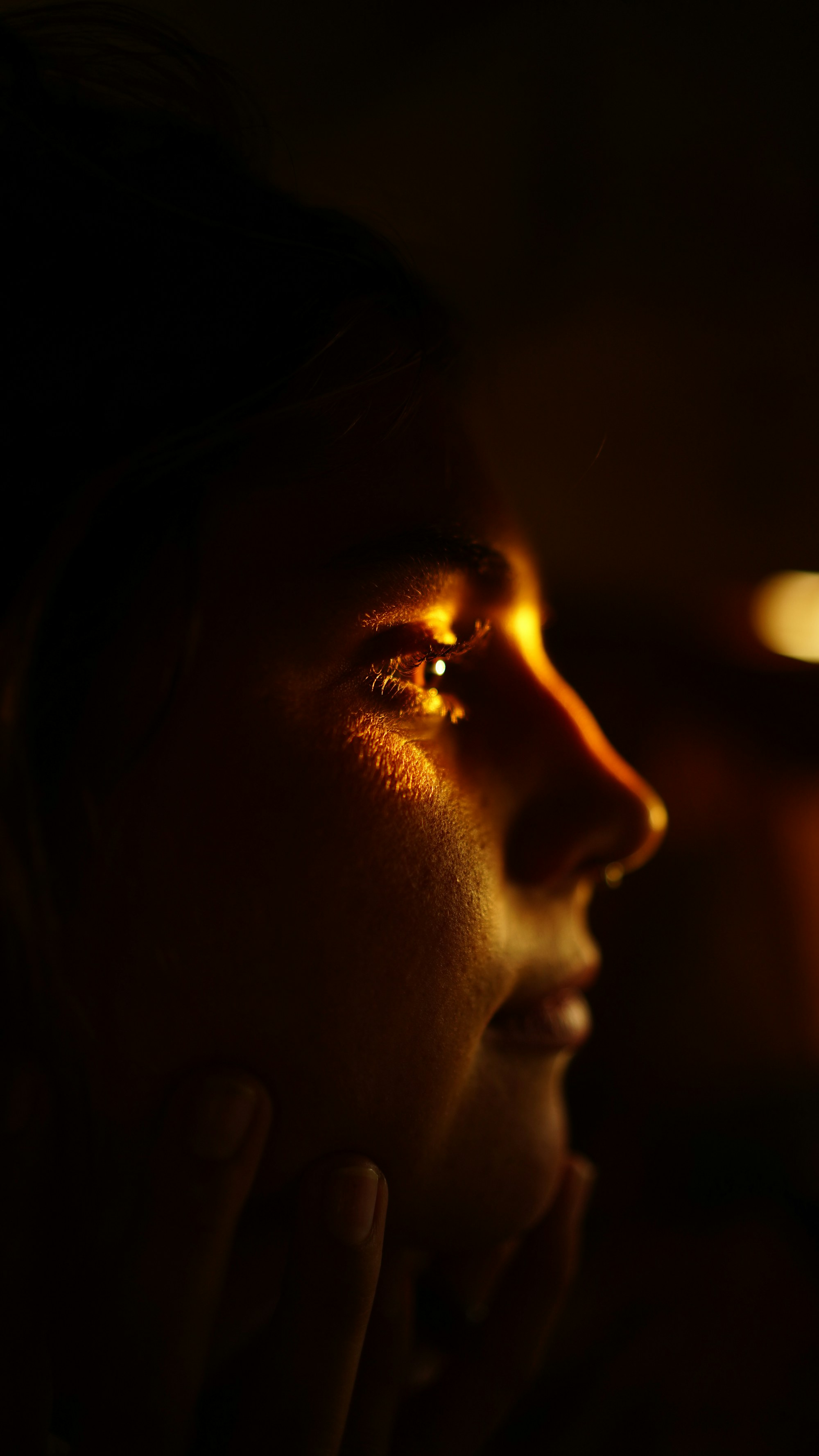 A face in profile lit by a single warm streak of light