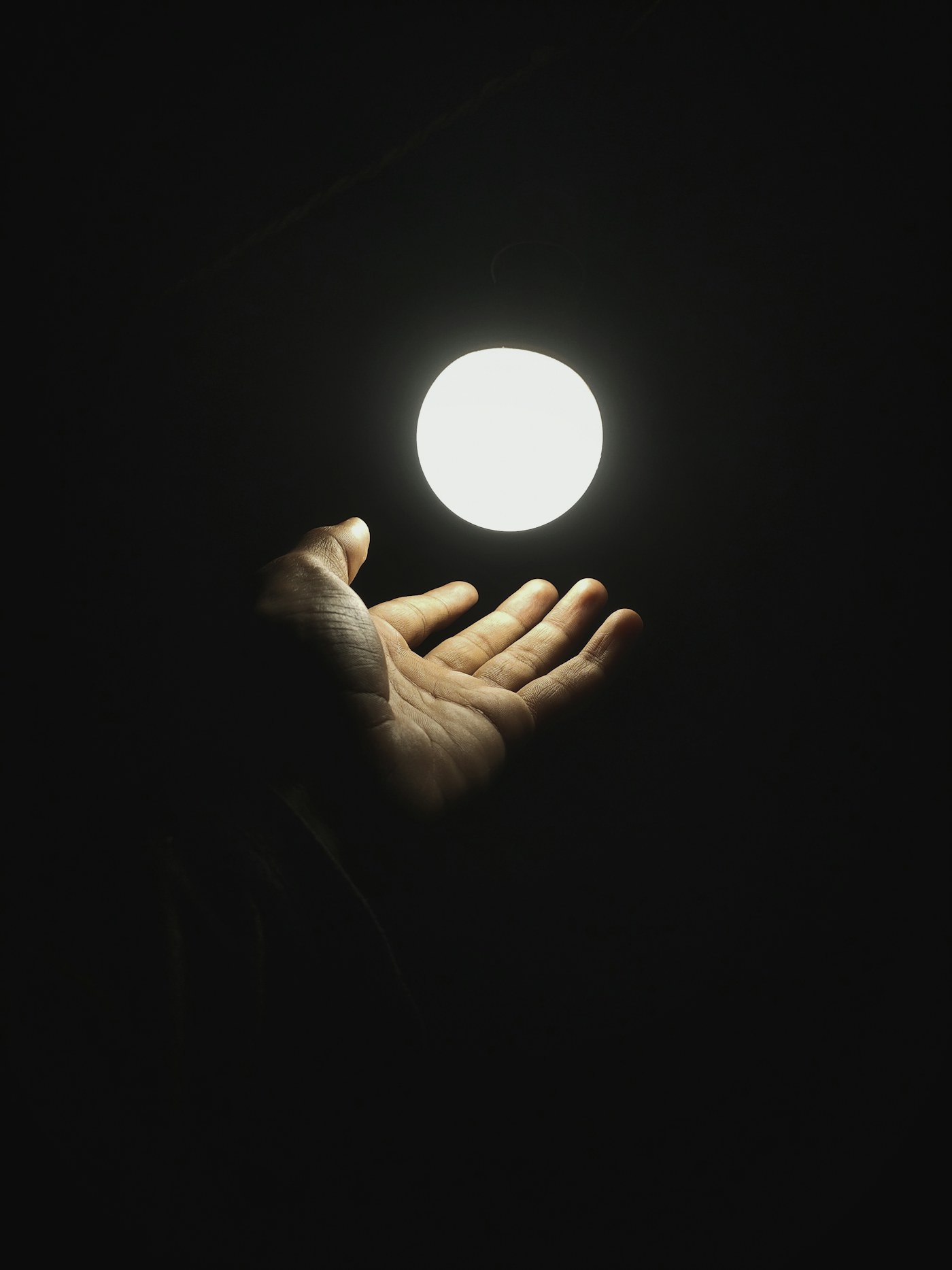 A hand holding a softly glowing orb of light in darkness